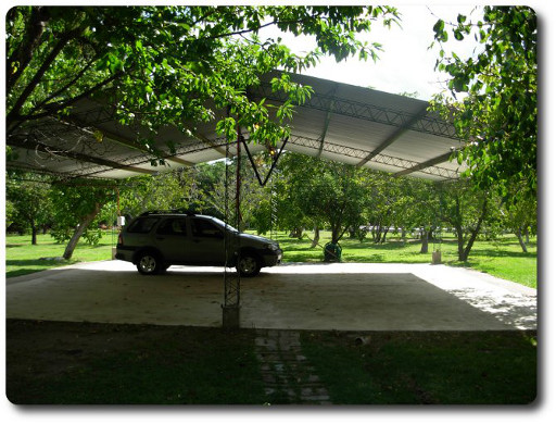 La foto muestra el primer plano la cochera cubierta y protegida del alojamiento para tranquilidad de los usuarios de la hostería, en un segundo plano se puede apreciar el gran parque arbolado.