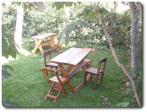 La foto muestra mesas y sillas sobre el pasto y entre los árboles para que los huéspedes puedan disfrutar de su desayuno y sus encuentros en contacto directo con el entorno natural de la hostería