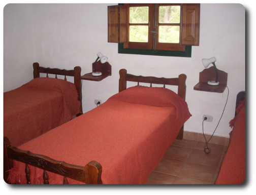 La foto muestra parte de una habitación de la hostería. En ella se pueden ver tres camas. La ventana da a parte del parque arbolado. Todas las camas tienen colchones Somier para su mejor descanso.