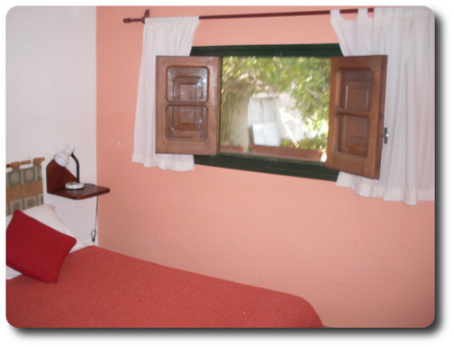 La foto muestra una de las habitaciones con TV LCD de la hostería. Sobre la cama está el control remoto y el TV LCD en una pared. Al fondo hay una cómoda, un sillón y el baño completamente instalado con todas las comodidades.