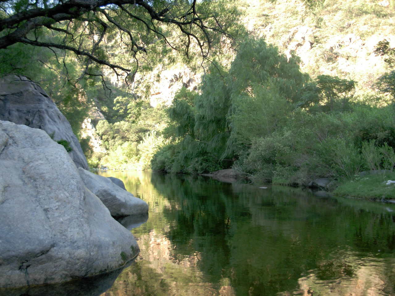 La foto muestra un primer plano del río San Marcos corriendo entre grandes piedras y árboles cerca de la hostería.
